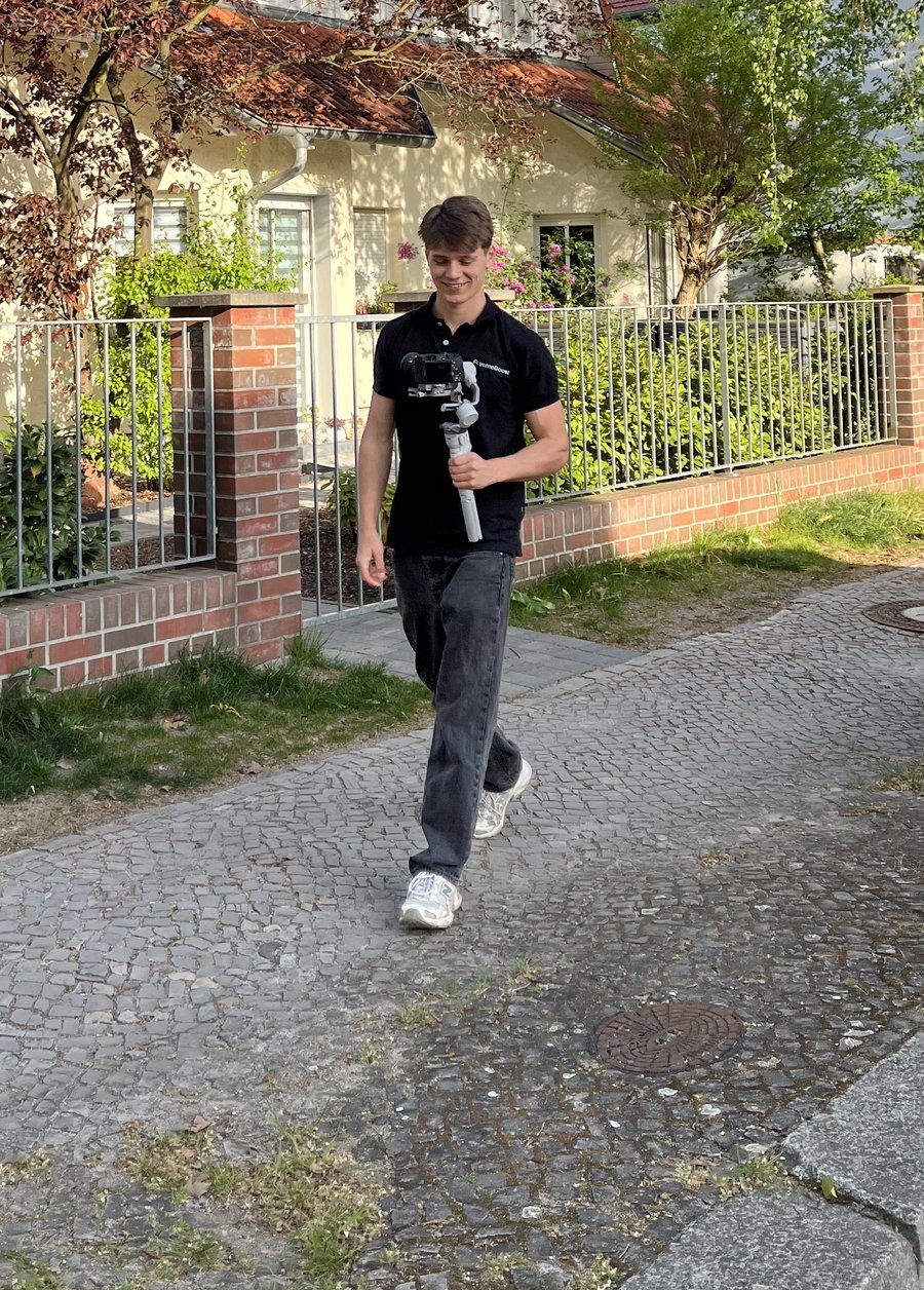 Felix walking towards the camera with a gimbal in front of a house